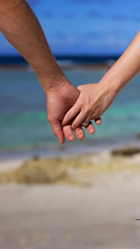 Ảnh hai người nắm tay nhau, bàn chân chạm nước biển