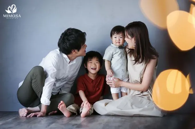 Gia đình 4 người bế con nhỏ ngồi trên thảm, cười rạng rỡ