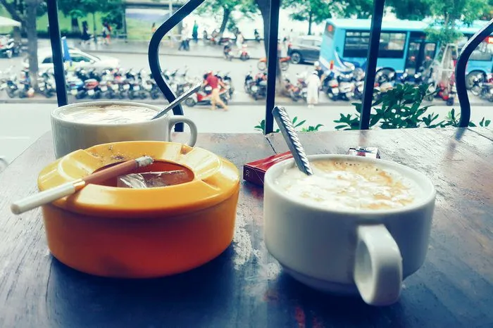 Ly cà phê và điếu thuốc đặt cạnh một chiếc bật lửa cũ, mang đến cảm giác hoài niệm và sâu lắng.