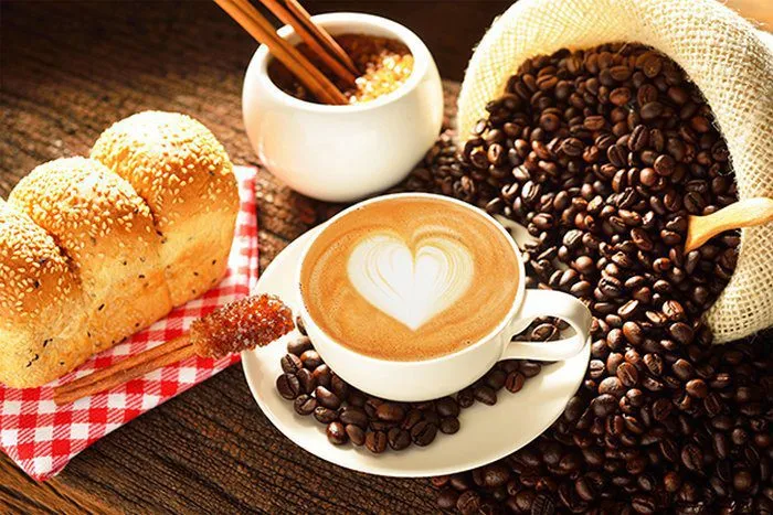 Ly cà phê tình yêu với hạt cà phê rải xung quanh, tạo nên khung cảnh lãng mạn và ngọt ngào.