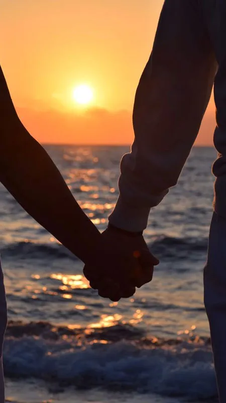 Bàn tay nam và nữ đan chặt, biểu tượng của tình yêu bền vững giữa khung cảnh biển trời