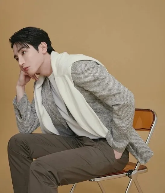 Một người mẫu nam trong bộ vest lịch lãm màu xám than, áo sơ mi trắng và cà vạt đen, tạo dáng tự tin và chuyên nghiệp.